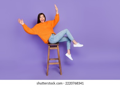 Full size photo of lovely young woman sit stool falling lean over dressed stylish orange knitted outfit isolated on purple color background