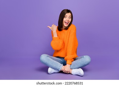 Full size photo of lovely young woman sit floor point copyspace dressed stylish orange knitted look isolated on purple color background - Shutterstock ID 2220768531