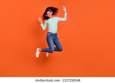 Full size photo of millennial lady jump listen music wear earphones shirt jeans shoes isolated on orange background