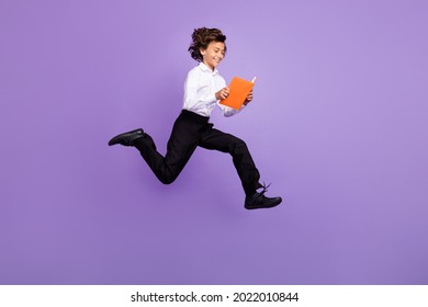 Full Size Photo Of Nice Little Brunet Boy Jump Read Book Wear Shirt Trousers Sneakers Isolated On Purple Color Background