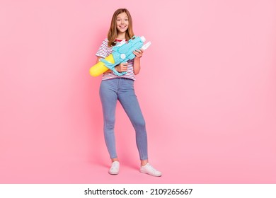 Full size photo of nice teen blond girl shoot from gun wear t-shirt jeans shoes isolated on pink background