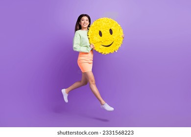 Full size photo of optimistic adorable woman wear sweatshirt flying hold big yellow smile emoji isolated on purple color background - Shutterstock ID 2331568223