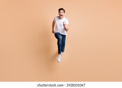 Full size photo of optimistic brunet man run yell wear t-shirt jeans sneakers isolated on beige color background