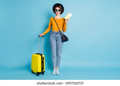 Full size photo of optimistic brunette short hairdo lady stand with bag tickets wear shirt jeans sneakers isolated on blue color background