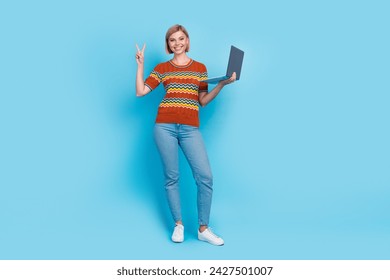Full size photo of optimistic cheerful woman dressed knit t-shirt hold laptop showing v-sign symbol isolated on blue color background