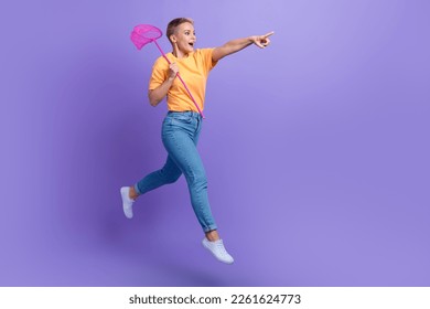 Full size photo of optimistic excited girl sneakers denim pants hold net directing empty space isolated on purple color background - Powered by Shutterstock