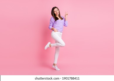 Full size photo of optimistic girl stand show v-sign wear lilac sweater trousers sneakers isolated on pink color background - Shutterstock ID 1901788411