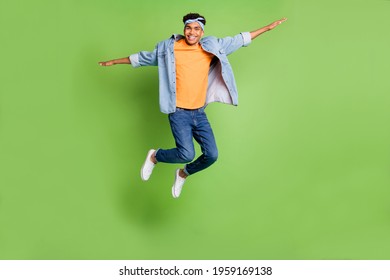 Full size photo of optimistic nice brunette guy jump wear blue shirt band jeans sneakers isolated on green color background