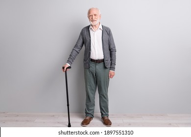 Full Size Photo Of Optimistic Old Man Stand With Stick Wear Dark Sweater Trousers Isolated On Grey Wall