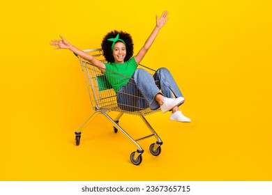 Full size photo of overjoyed carefree girl sit inside market trolley raise hands empty space isolated on yellow color background - Shutterstock ID 2367365715
