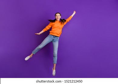 Full Size Photo Of Positive Cheerful Teen Girl Hold Hand Jump Catch Her Flying Parasol On Windy Weather Wear Orange Sporty Outfit Jeans White Sneakers Isolated Over Violet Purple Color Background