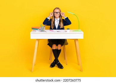 Full Size Photo Of Positive Girl With Straight Hairdo Dressed Blue Jacket Sit At Desk Touch Glasses Isolated On Yellow Color Background