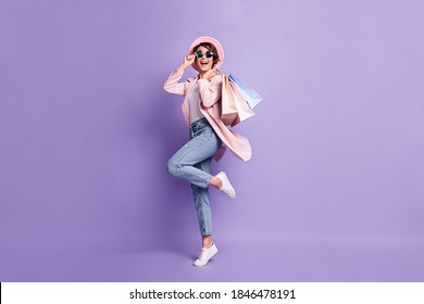 Full size photo of positive pretty girl jump hold purchases wear glasses coat jeans shoes isolated on purple background