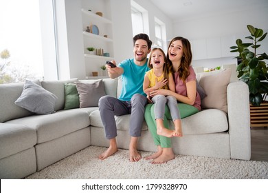 Full size photo of positive three people mom dad preteen little kid girl sit comfort couch rest watch comedy cartoon remote control switch joy laugh in house indoors