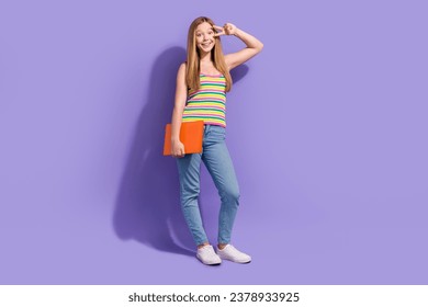 Full size photo of pretty teenager blonde girl hold laptop show v-sign hi wear trendy striped outfit isolated on purple color background