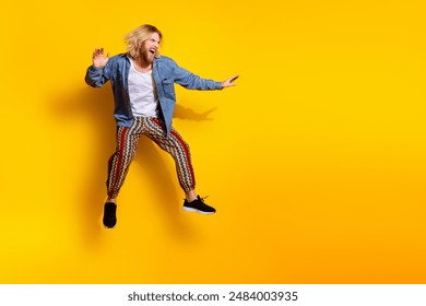 Full size photo of pretty young guy jump keep balance surfing wear trendy jeans outfit isolated on yellow color background - Powered by Shutterstock