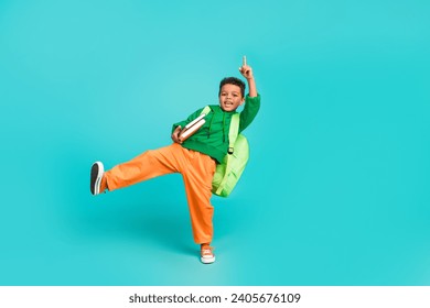 Full size photo of small boy with rucksack wear green hoodie hold book directing up at empty space isolated on turquoise color background - Powered by Shutterstock