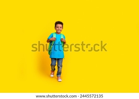 Full size photo of smart little boy wear casual blue t-shirt denim pants rucksack back to school isolated on vivid yellow background