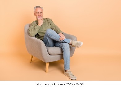 Full Size Photo Of Strict Old Grey Hairdo Man Sit Wear Eyewear Pullover Jeans Footwear Isolated On Beige Background