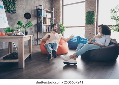 Full size photo of two young colleagues sit beanbag chatting loft interior office business center indoors - Powered by Shutterstock