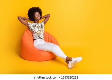Full size photo of young afro beautiful positive cheerful girl woman sit orange armchair relax enjoy isolated on yellow color background