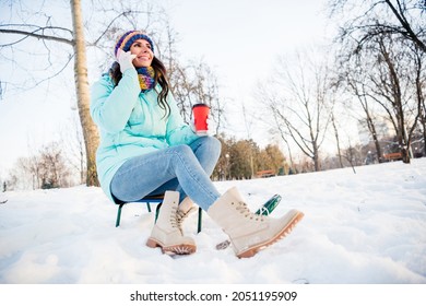 Full size photo of young beautiful charming positive girl drinking coffee talking on phone sit sledge in winter park forest - Powered by Shutterstock