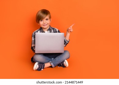 Full size photo of young boy indicate finger empty space recommend promo laptop isolated over orange color background - Powered by Shutterstock