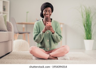 Full size photo of young cheerful black girl happy positive smile sit floor home lotus pose chat type sms cellphone