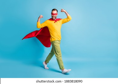 Full size photo of young handsome powerful superhero go walk showing muscles biceps isolated on blue color background