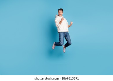 Full size photo of young happy excited crazy positive man jumping hold fists in victory isolated on blue color background