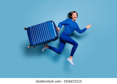 Full size photo of young happy positive good mood smiling girl run jump hold big luggage isolated on blue color background