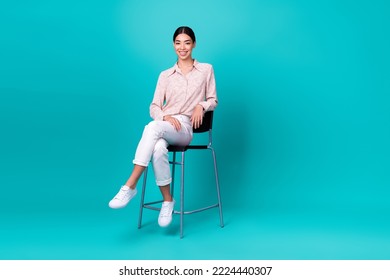 Full size photo of young korean lady sit bar chair relaxing toothy smile wear stylish smart casual outfit isolated on cyan color background