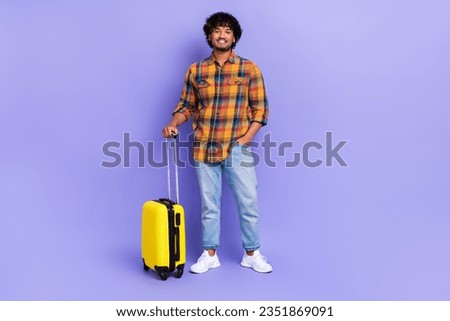 Full size photo of young traveler guy enjoy world trip wear checkered shirt with yellow suitcase isolated over purple color background