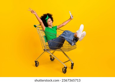 Full size portrait of beautiful teen girl sit market pushcart hold smart phone make selfie show v-sign isolated on yellow color background - Shutterstock ID 2367365713