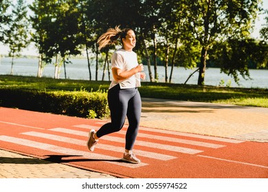 Full Size Portrait Of A Body Positive Plus-size Plump Woman Athlete Jogging Running In Fitness Outfit, Losing Weight While Listening To Music In Stadium Outdoors