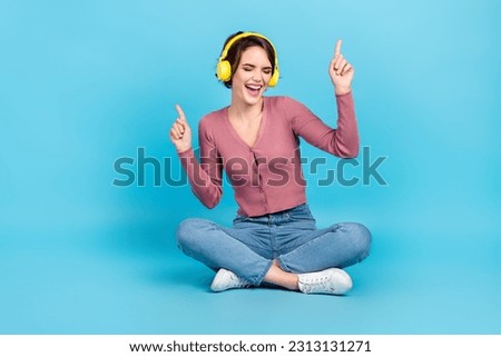 Full size portrait of carefree overjoyed girl sit floor point fingers enjoy favorite playlist isolated on blue color background