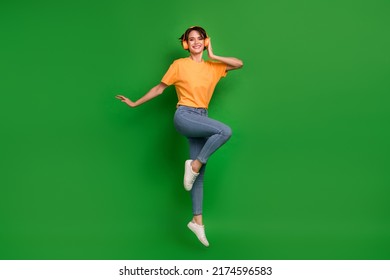Full size portrait of cheerful pretty person jump arm touch headphones enjoy music isolated on green color background