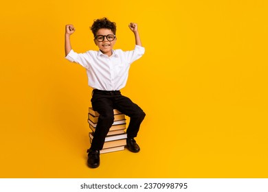 Full size portrait of delighted smart little boy sit pile stack book raise fists empty space isolated on yellow color background - Powered by Shutterstock