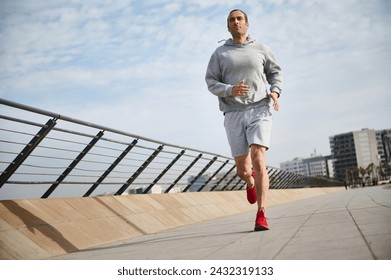 Full size portrait of handsome mid adult sportsman, athletic man running on the bridge on sunny day, enjoying his morning jog on the promenade. Active people. Sport. Cardio workout. Healthy lifestyle - Powered by Shutterstock