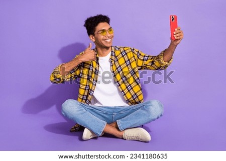 Full size portrait of positive nice person sit floor hold smart phone make selfie demonstrate thumb up isolated on purple color background