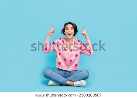 Full size portrait of pretty astonished girl sit floor crossed legs indicate fingers up empty space isolated on blue color background