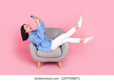 Full size portrait of pretty girl sit chair hold use smart phone chatting isolated on pink color background - Powered by Shutterstock