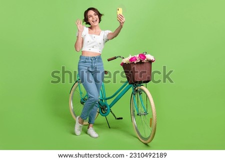 Full size portrait of pretty girl hold smart phone make selfie video call arm waving hi flower basket bicycle isolated on green color background