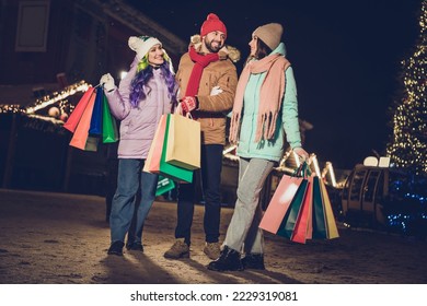 Full size portrait of three positive carefree people hold packages chatting enjoy free time evening outside