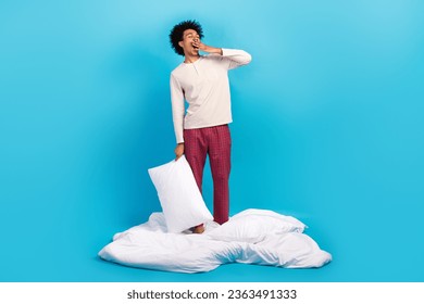 Full size portrait of tired funky person stand cozy blanket arm hold pillow cover mouth yawning isolated on blue color background - Powered by Shutterstock