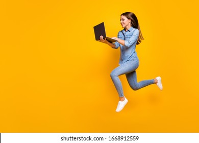 Full size profile photo of beautiful business lady jump high hold notebook hands hurry work browsing laptop wear casual denim outfit white sneakers isolated yellow color background