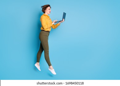 Full size profile photo of beautiful lady jumping high up holding browsing notebook workaholic wear yellow shirt green pants shoes isolated bright blue color background - Shutterstock ID 1698450118