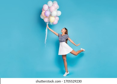 Full size profile photo of beautiful funky lady hold many colorful balloons fly up wind blowing wear striped t-shirt white short skirt footwear isolated blue color background