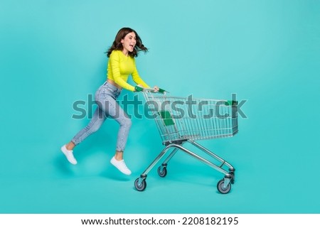 Full size profile photo of cool brunette hair young lady run with trolley wear shirt jeans sneakers isolated on teal color background