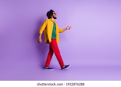 Full size profile photo of dark skin man walking look empty space toothy smile isolated on violet color background